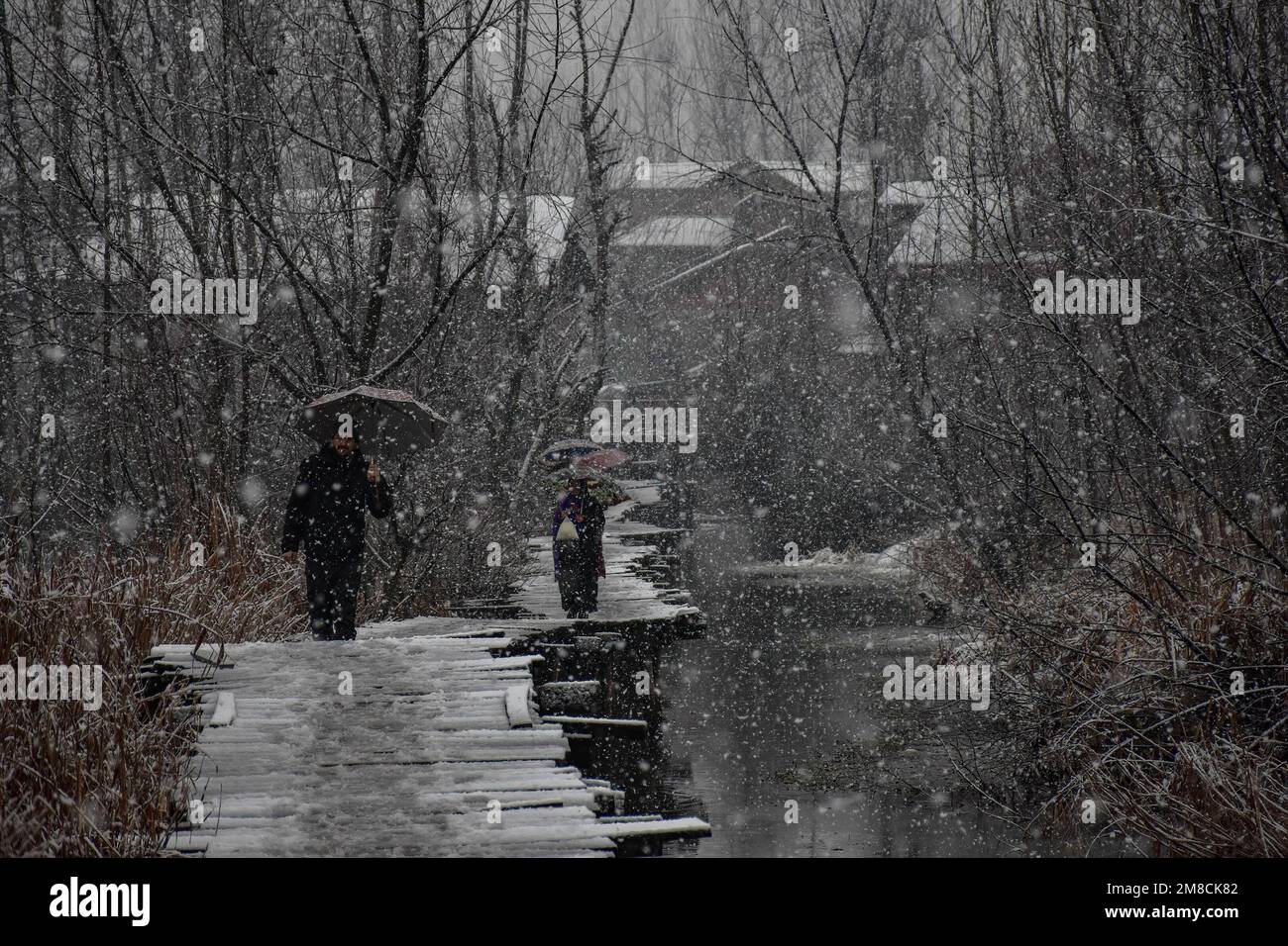 I residenti camminano lungo il ponte pedonale in legno durante le nevicate. Parti della valle di Kashmir compreso Srinagar ha ricevuto nevicate che portano alla chiusura della vitale Srinagar-Jammu autostrada nazionale e la cancellazione delle operazioni di volo, funzionari qui ha detto. Foto Stock