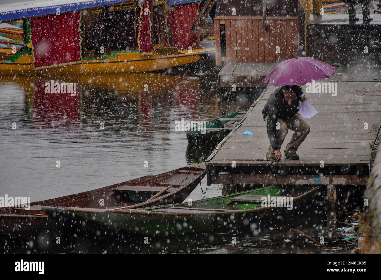 Un barcaiolo lega la sua barca alle rive del lago dal durante le nevicate. Parti della valle di Kashmir compreso Srinagar ha ricevuto nevicate che portano alla chiusura della vitale Srinagar-Jammu autostrada nazionale e la cancellazione delle operazioni di volo, funzionari qui ha detto. Foto Stock