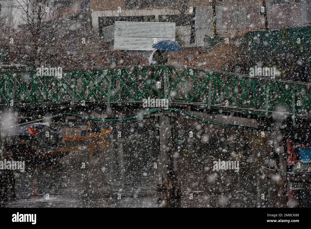 Un residente tiene un ombrello mentre cammina attraverso il ponte pedonale di legno durante le nevicate. Parti della valle di Kashmir compreso Srinagar ha ricevuto nevicate che portano alla chiusura della vitale Srinagar-Jammu autostrada nazionale e la cancellazione delle operazioni di volo, funzionari qui ha detto. Foto Stock