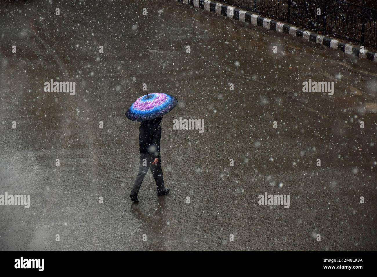 Un uomo tiene un ombrello mentre cammina per la strada durante le nevicate. Parti della valle di Kashmir compreso Srinagar ha ricevuto nevicate che portano alla chiusura della vitale Srinagar-Jammu autostrada nazionale e la cancellazione delle operazioni di volo, funzionari qui ha detto. Foto Stock