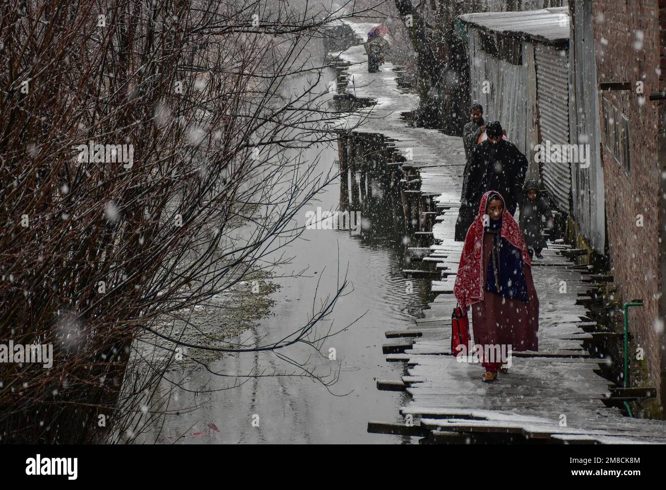 I residenti camminano lungo il ponte pedonale in legno durante le nevicate. Parti della valle di Kashmir compreso Srinagar ha ricevuto nevicate che portano alla chiusura della vitale Srinagar-Jammu autostrada nazionale e la cancellazione delle operazioni di volo, funzionari qui ha detto. Foto Stock
