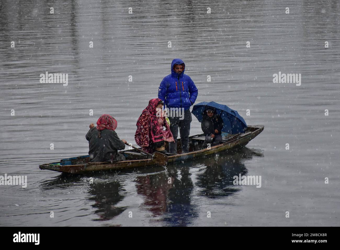 Una donna ferry la sua famiglia in una barca durante la nevicata. Parti della valle di Kashmir compreso Srinagar ha ricevuto nevicate che portano alla chiusura della vitale Srinagar-Jammu autostrada nazionale e la cancellazione delle operazioni di volo, funzionari qui ha detto. Foto Stock