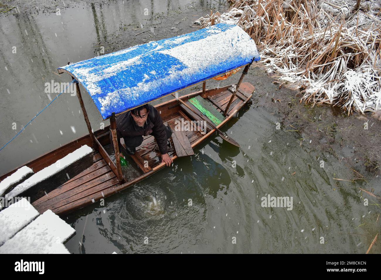 Un barcaiolo rimuove l'acqua dalla sua barca durante le nevicate. Parti della valle di Kashmir compreso Srinagar ha ricevuto nevicate che portano alla chiusura della vitale Srinagar-Jammu autostrada nazionale e la cancellazione delle operazioni di volo, funzionari qui ha detto. Foto Stock