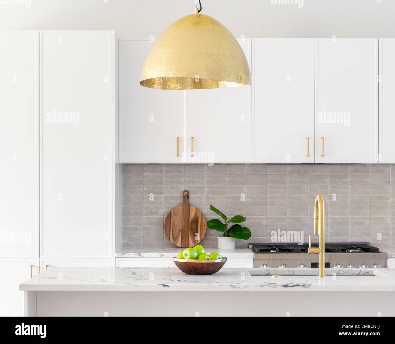 Un particolare cucina con armadi bianchi, rubinetto d'oro e luce che pende sull'isola, e un backsplash piastrellato. Foto Stock