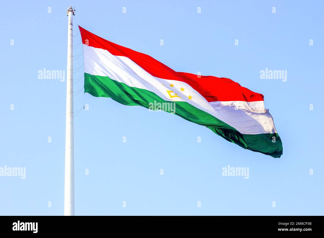 Bandiera nazionale rossa, bianca e verde del Tagikistan sul paletto contro il cielo blu. Foto Stock