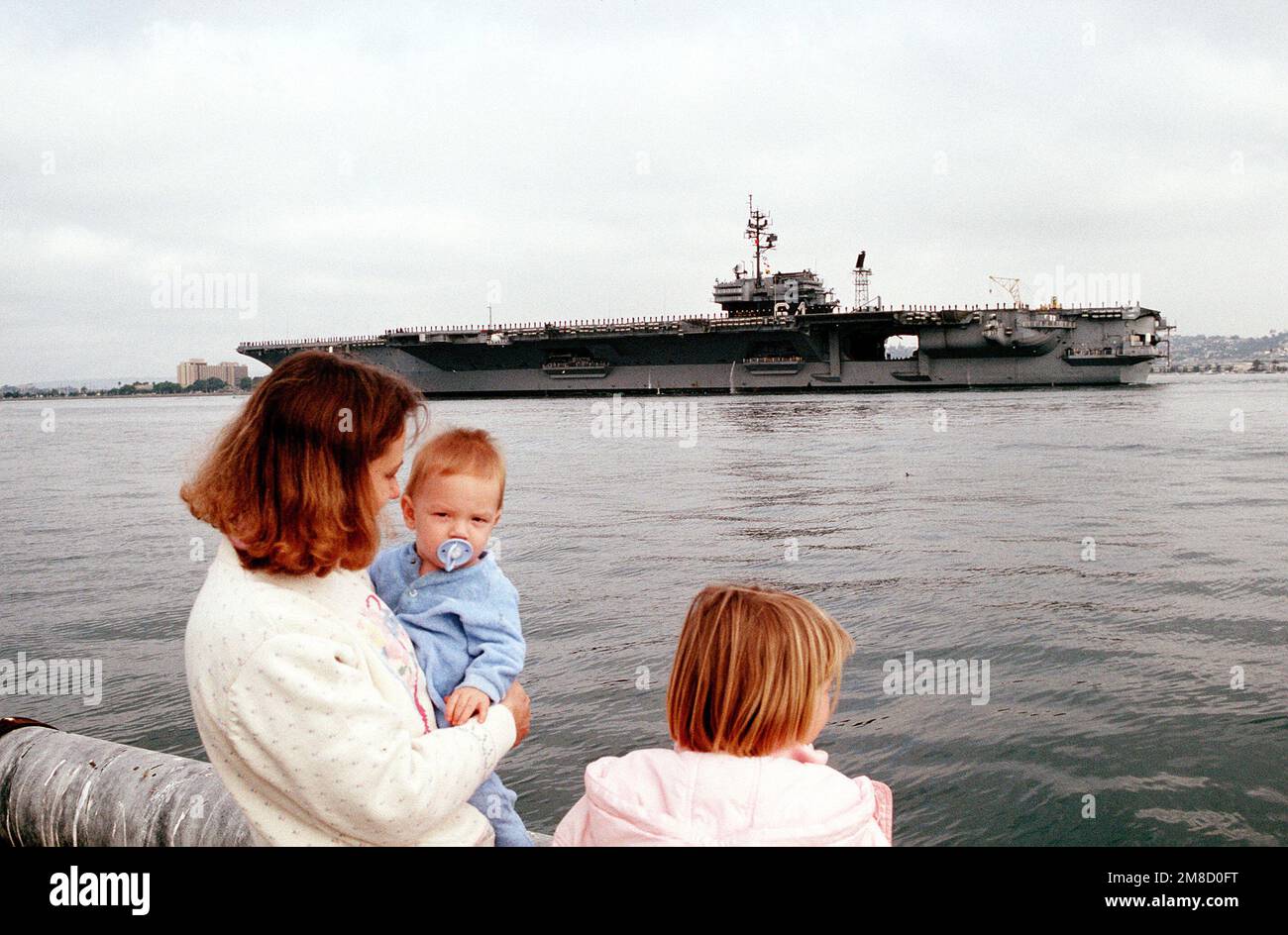 Una famiglia attende sul molo mentre la portaerei USS CONSTELLATION (CV-64), membri dell'equipaggio che presergono le rotaie, si prepara ad attraccare. Base: San Diego Stato: California (CA) Paese: Stati Uniti d'America (USA) Foto Stock