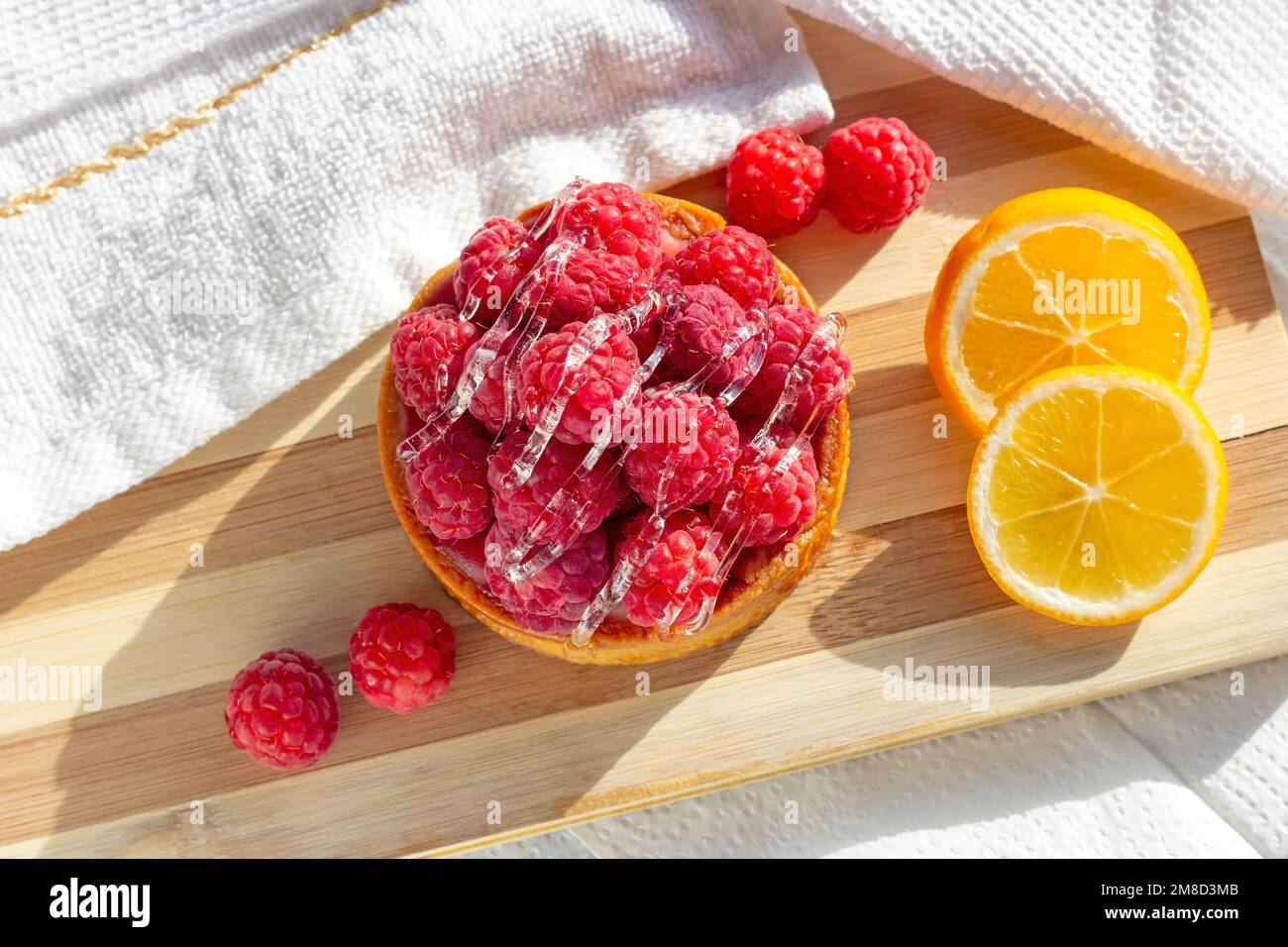 Vista dall'alto della crostata rosa di lamponi freschi e dei limoni freschi sullo sfondo del tavolo da cucina. Foto Stock