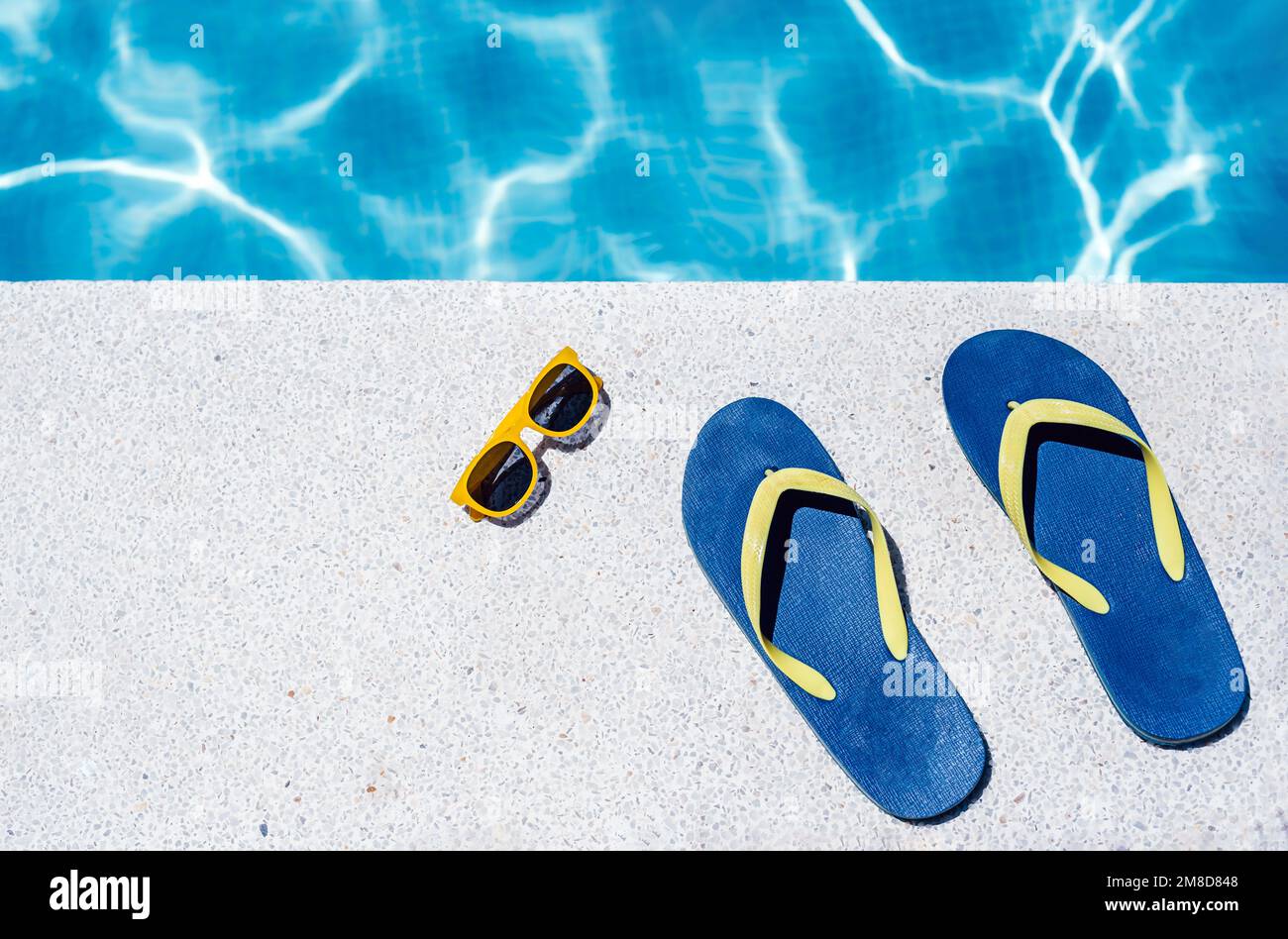 vista zenith di infradito e occhiali sul bordo bianco di una piscina con acqua bluastra sullo sfondo. vacanza e concetto di estate. Foto Stock