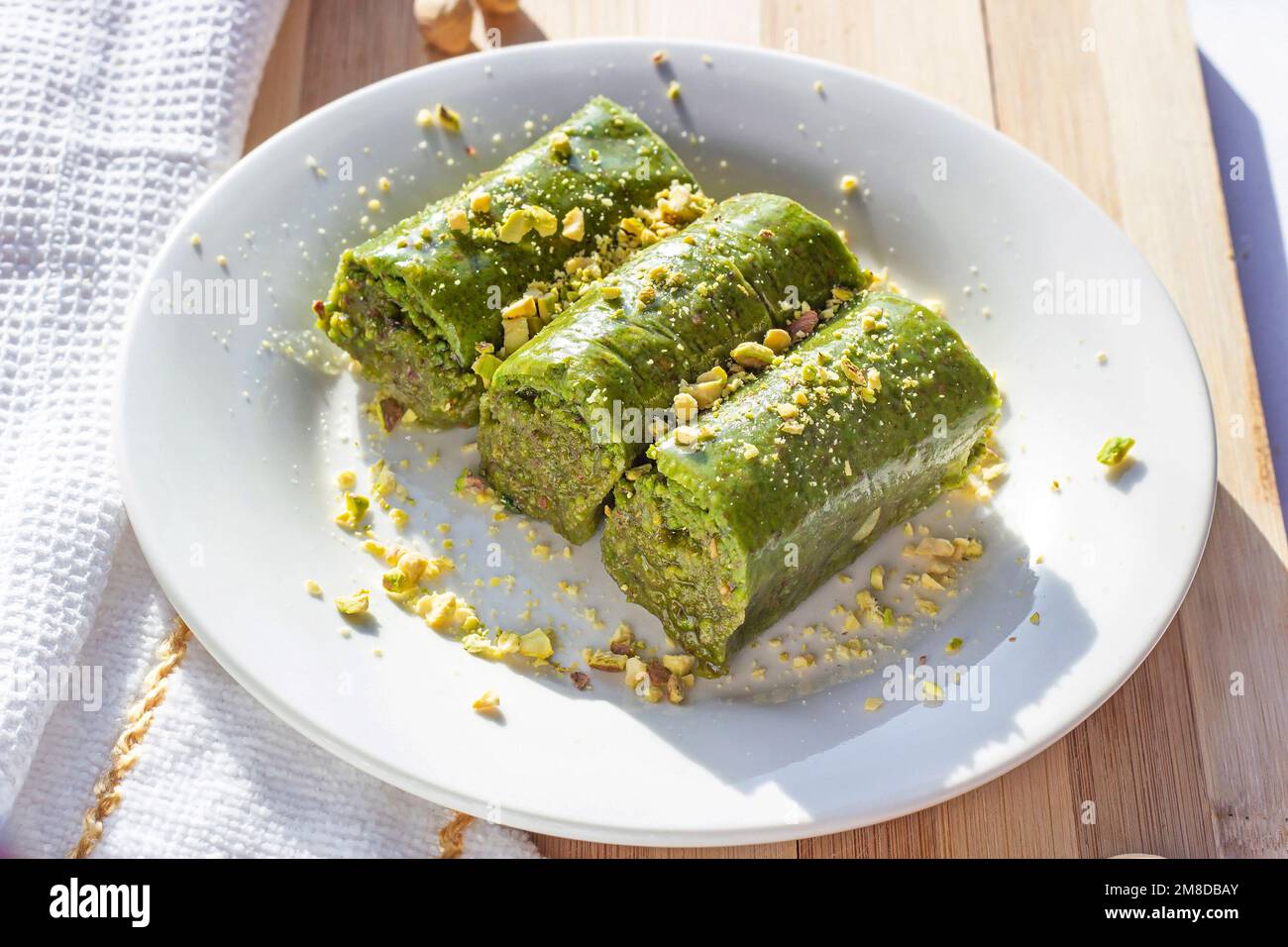 Tradizionale panbaklava di pistacchio o pahlava dolce dell'Asia orientale con noci e sciroppo su un piatto bianco su fondo di legno chiaro. Foto Stock
