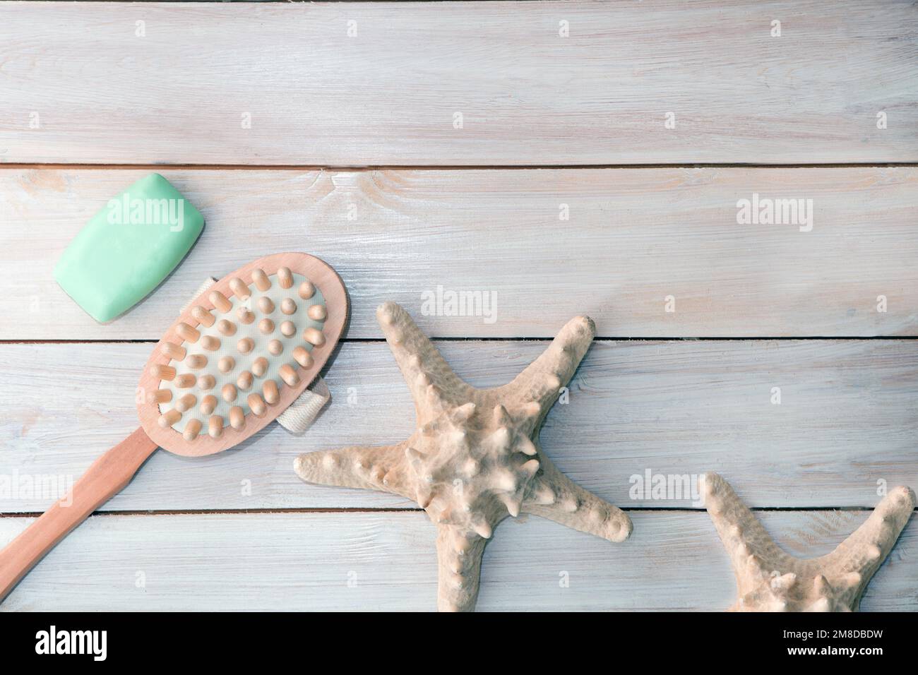 Spazzola massaggiante, sapone, stelle marine su sfondo di legno chiaro Foto Stock