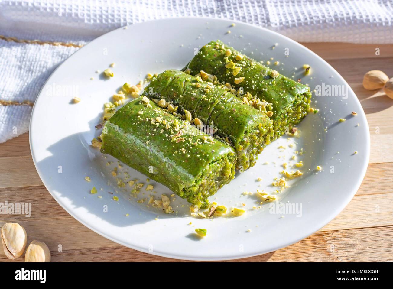 Tradizionale panbaklava di pistacchio o pahlava dolce dell'Asia orientale con noci e sciroppo su un piatto bianco su fondo di legno chiaro. Foto Stock