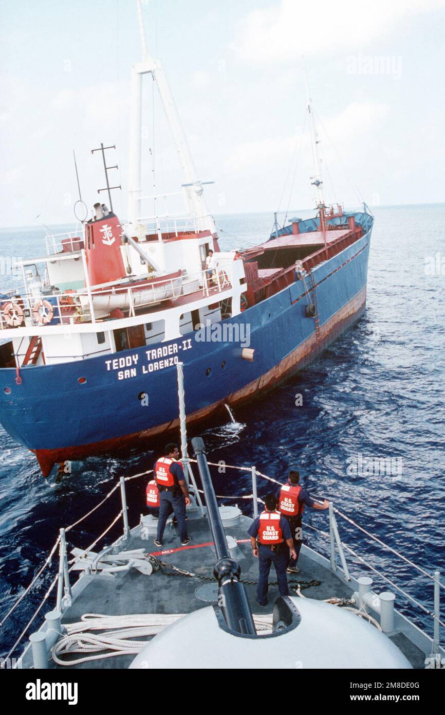 In piedi di fronte alla pistola Mark da 75 76 mm sulla prua di una nave missilistica combattente per la pattuglia con aliscafo, una squadra di polizia della Guardia Costiera si prepara a salire a bordo della nave commerciale TEDDY TRADER II per un'ispezione. Paese: Sconosciuto Foto Stock