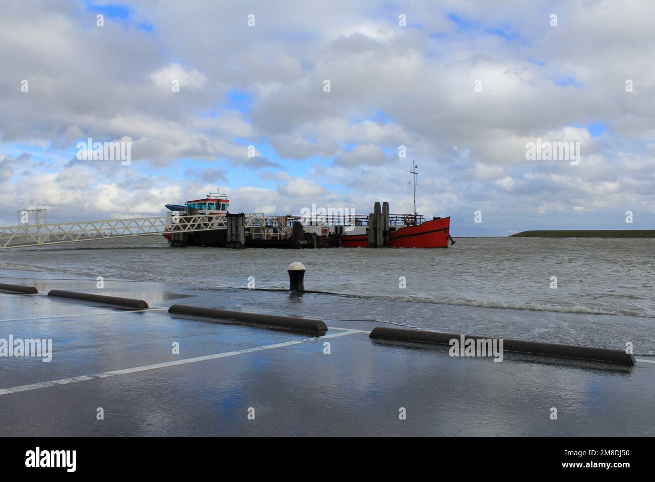 una nave rossa è ormeggiata mentre il mare è in aumento e corre sulla riva con la prossima alta marea e forza eolica 9 al westerschelde in olanda in wint Foto Stock