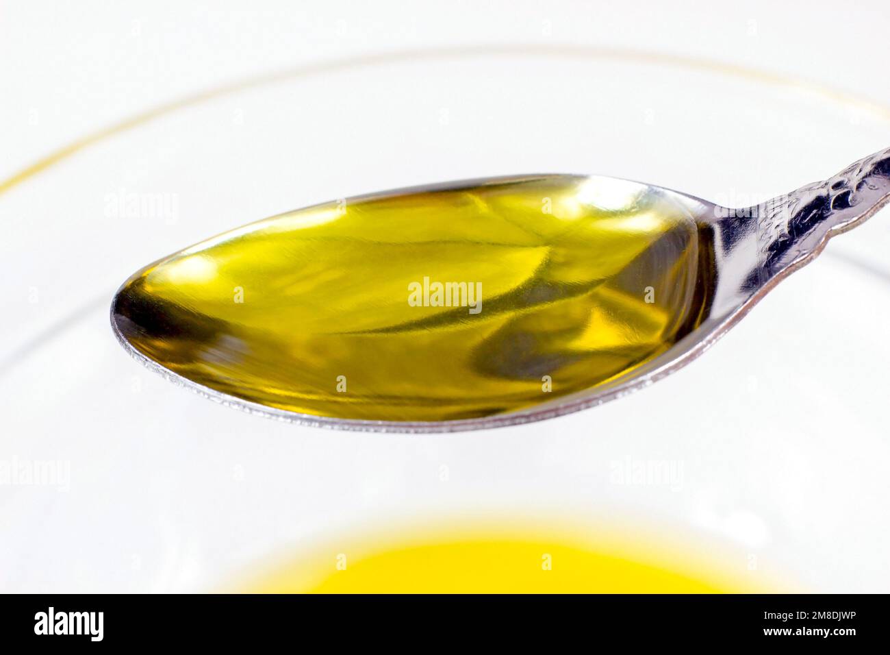 Olio d'oliva biologico giallo nel cucchiaio su fondo chiaro primo piano. Foto Stock