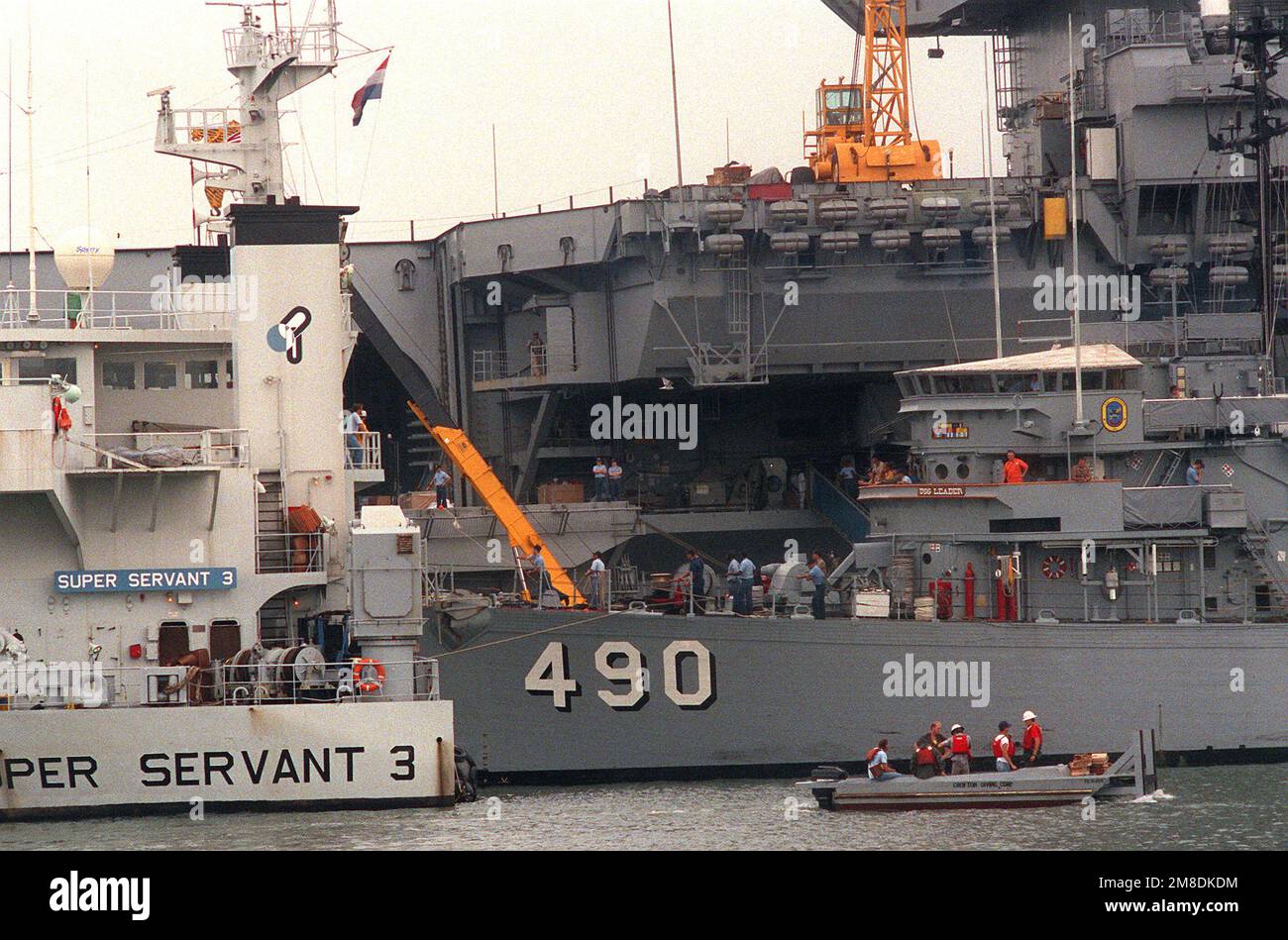 Il LEADER USS (MSO-490) è legato al ponte sommerso della nave pesante olandese SUPER SERVER 3. Il SUPER SERVITORE 3 porterà il LEADER, altri due minatori oceanici e una nave di contromisure minerarie al Golfo Persico, dove le forze statunitensi stanno operando in risposta all'invasione del Kuwait da parte dell'Iraq. La portaerei a energia nucleare USS ENTERPRISE (CVN-65) è in secondo piano. Base: Naval Air Station, Norfolk Stato: Virginia (VA) Paese: Stati Uniti d'America (USA) Foto Stock