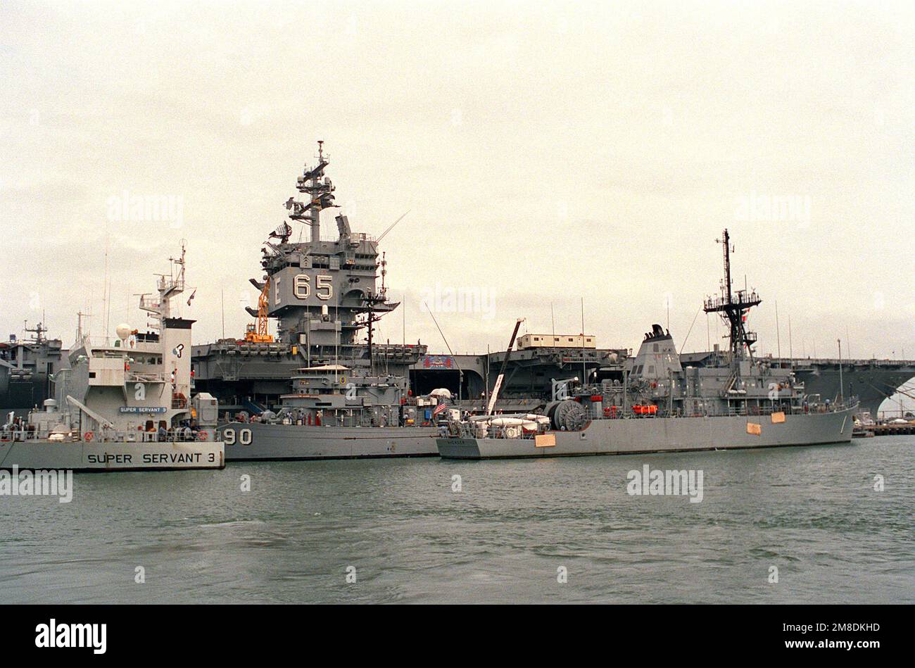 La nave USS AVENGER (MCM-1), a destra, viene tirata in posizione accanto al LEADER USS (MSO-490), che si trova sul ponte sommerso della nave pesante olandese SUPER SERVOR 3. Il SUPER SERVITORE 3 porterà il VENDITORE, IL LEADER e altri due minatori oceanici nel Golfo Persico, dove le forze statunitensi stanno operando in risposta all'invasione del Kuwait da parte dell'Iraq. La portaerei a energia nucleare USS ENTERPRISE (CVN-65) è in secondo piano. Base: Naval Air Station, Norfolk Stato: Virginia (VA) Paese: Stati Uniti d'America (USA) Foto Stock
