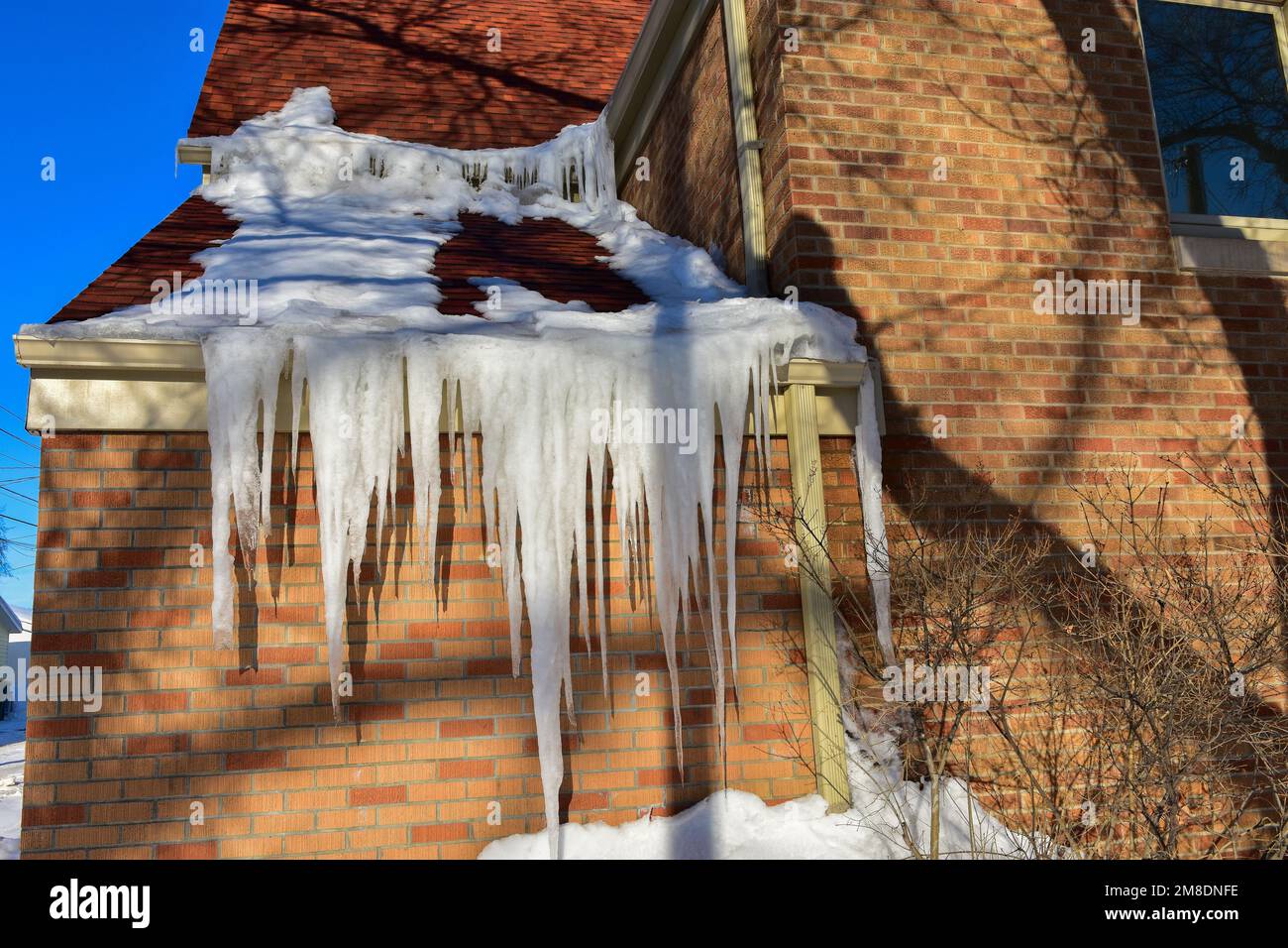 Sciogliendo neve sul tetto creando diga di ghiaccio in grondaia e ghiaccioli che tirano giù sulla grondaia. Foto Stock