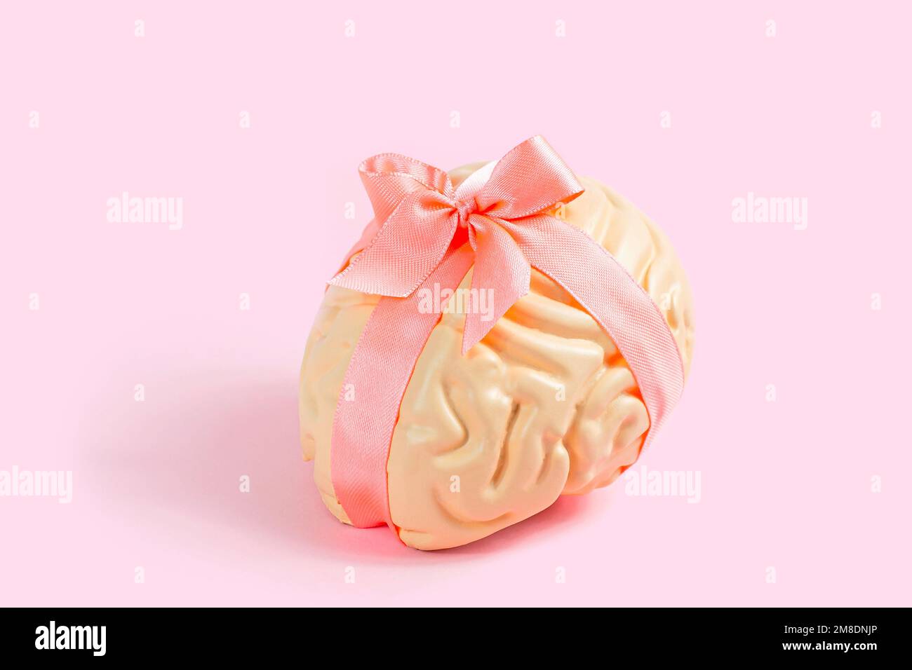 Modello a cervello umano rosa brillante con arco in raso su sfondo pastello. Creatività, ispirazione e concetto di salute mentale. Foto Stock