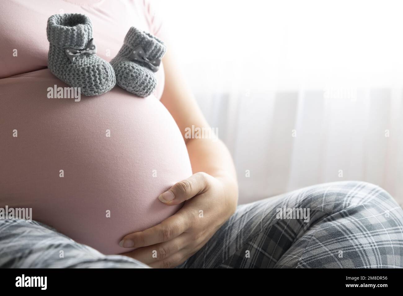 Donna incinta in t-shirt rosa che tocca il ventre. Due stivaletti di lana sul ventre. Gravidanza sana Foto Stock