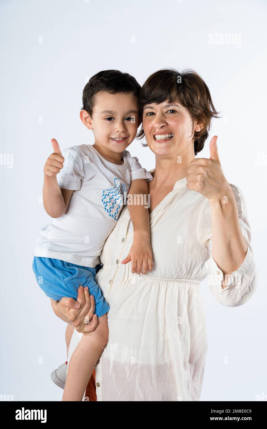 Giovane madre e figlio in piedi insieme su sfondo bianco facendo felice pollice su mano gesto. approvazione dell'espressione guardando la telecamera che mostra il successo Foto Stock