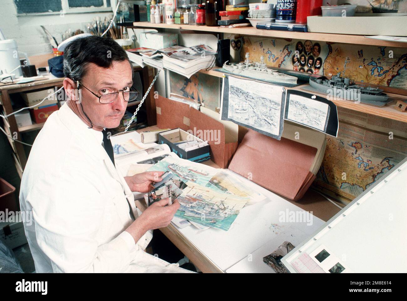 Artista di combattimento della marina CMDR. John Charles Roach, USNR-R, ordina le fotografie da utilizzare come soggetti per la pittura nel suo negozio al Washington Navy Yard. Roach sta facendo una serie di dipinti sull'operazione Desert Shield/Desert Storm. Subject Operation/Series: DESERT SHIELD DESERT STORM base: Washington Stato: District of Columbia (DC) Paese: Stati Uniti d'America (USA) Foto Stock