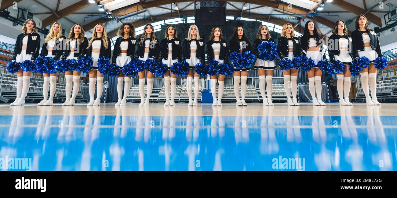 Vista ad angolo basso delle cheerleaders in mini-gonne in piedi in fila con pom-pom. Foto Stock