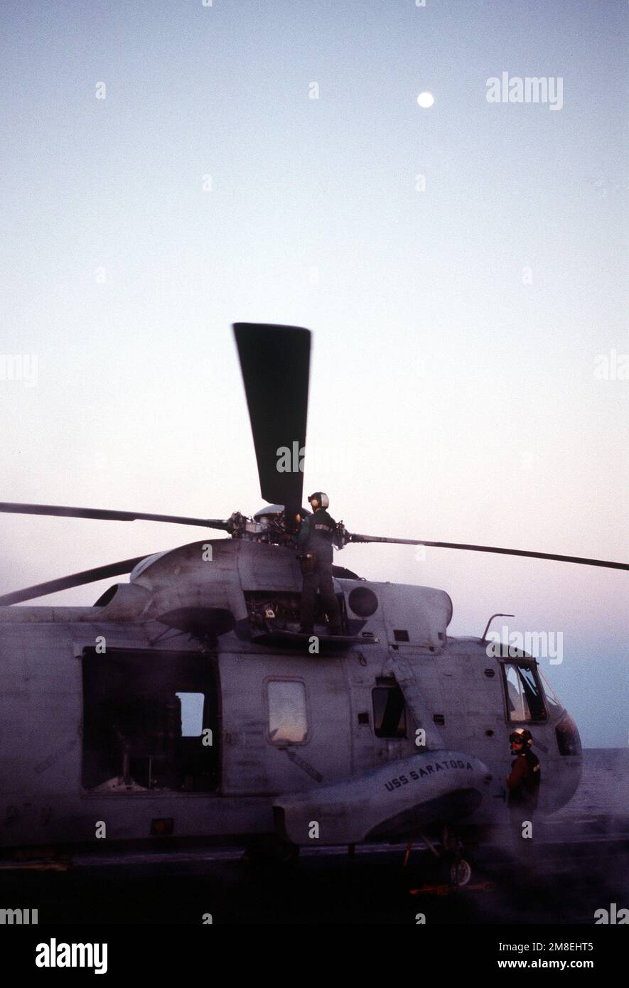 Un addetto alla manutenzione controlla una pala del rotore principale su un elicottero anti-sottomarino Squadron 3 (HS-3) SH-3H Sea King elicottero sul ponte di volo della portaerei USS SARATOGA (CV-60) durante l'operazione Desert Storm. Soggetto operativo/Serie: DESERT STORM Paese: Mar Rosso Foto Stock