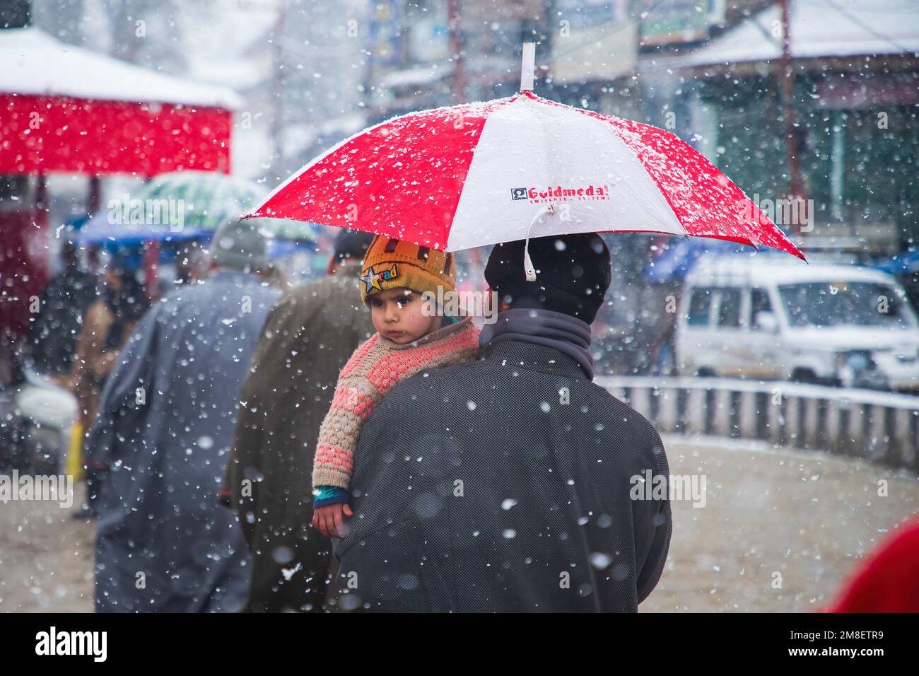 Un uomo di Kashmiri trasporta il suo bambino mentre cammina attraverso una strada in mezzo a nevicate pesanti in corso alla periferia di Srinagar. Almeno due operai uccisi il giovedì dopo che una valanga colpisce la zona ad alta quota nel Sonamerg del Kashmir centrale. La maggior parte delle parti del Kashmir ha ricevuto nevicate fresche che hanno portato alla chiusura della principale autostrada della capitale del Kashmir che collega la regione contesa con il resto dell'India. Nel frattempo, le autorità aeroportuali hanno sospeso tutte le operazioni di volo fino a nuovo avviso a causa della continua nevicata e della scarsa visibilità. Foto Stock