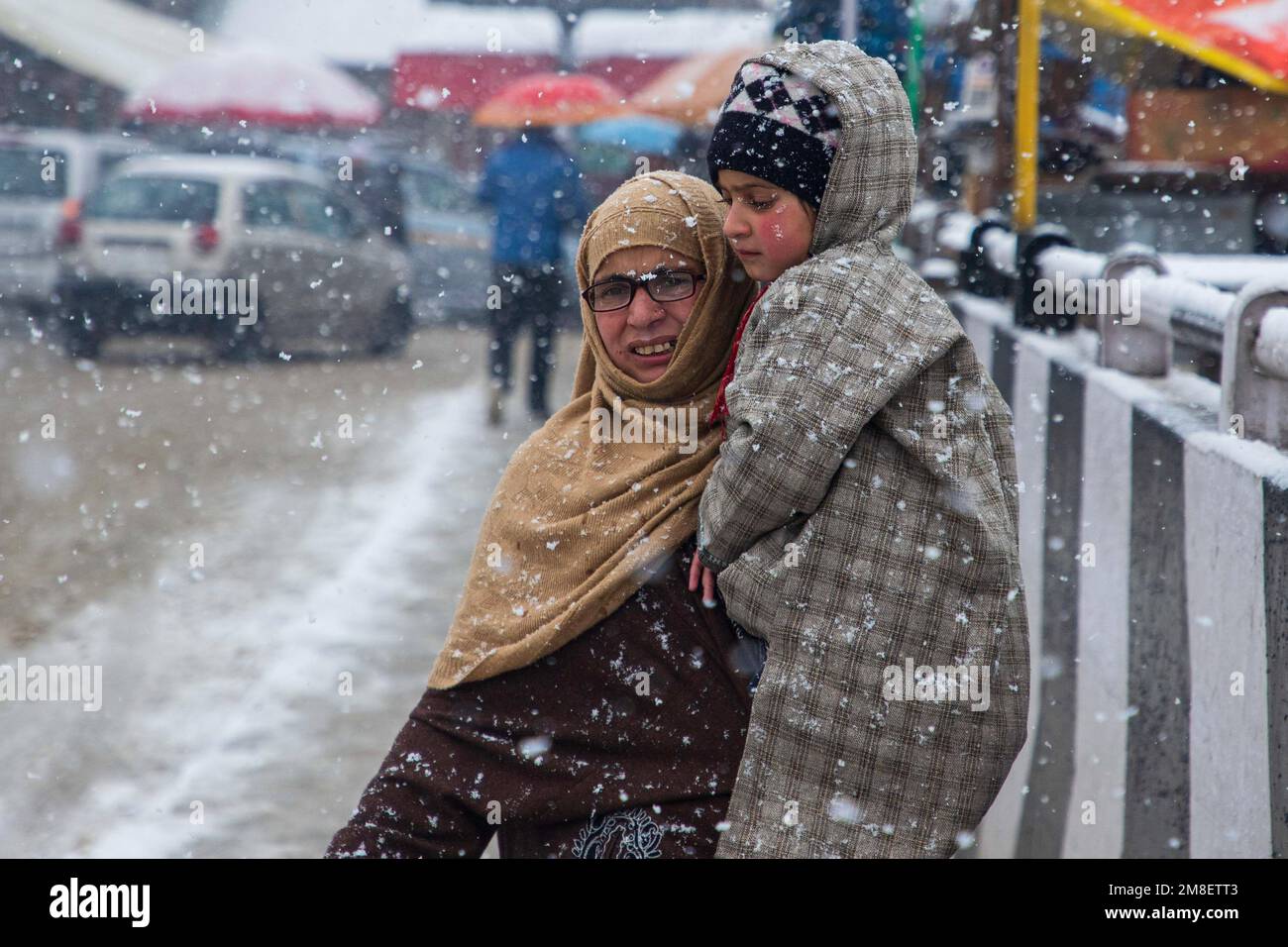 Una donna di Kashmiri trasporta il suo bambino mentre cammina attraverso una strada in mezzo a nevicate pesanti in corso alla periferia di Srinagar. Almeno due operai uccisi il giovedì dopo che una valanga colpisce la zona ad alta quota nel Sonamerg del Kashmir centrale. La maggior parte delle parti del Kashmir ha ricevuto nevicate fresche che hanno portato alla chiusura della principale autostrada della capitale del Kashmir che collega la regione contesa con il resto dell'India. Nel frattempo, le autorità aeroportuali hanno sospeso tutte le operazioni di volo fino a nuovo avviso a causa della continua nevicata e della scarsa visibilità. Foto Stock