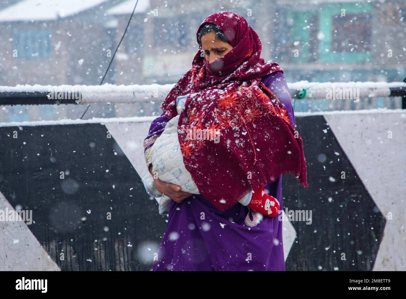 Una donna di Kashmiri trasporta il suo bambino mentre cammina attraverso una strada in mezzo a nevicate pesanti in corso alla periferia di Srinagar. Almeno due operai uccisi il giovedì dopo che una valanga colpisce la zona ad alta quota nel Sonamerg del Kashmir centrale. La maggior parte delle parti del Kashmir ha ricevuto nevicate fresche che hanno portato alla chiusura della principale autostrada della capitale del Kashmir che collega la regione contesa con il resto dell'India. Nel frattempo, le autorità aeroportuali hanno sospeso tutte le operazioni di volo fino a nuovo avviso a causa della continua nevicata e della scarsa visibilità. Foto Stock