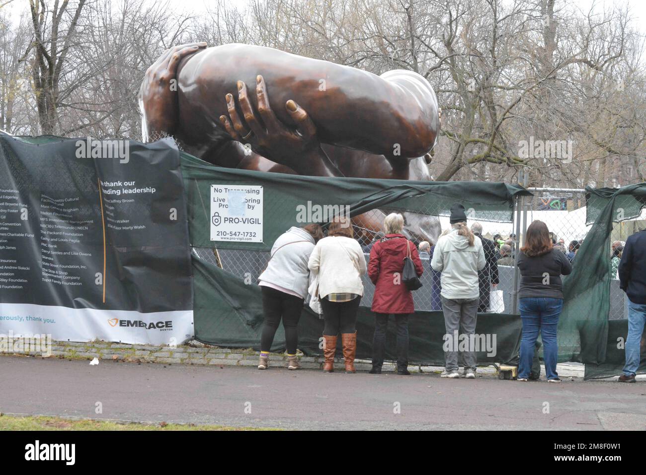 Boston, Massachusetts, Stati Uniti. 14th Jan, 2023. I Botoniani si riuniscono su Boston Common per la presentazione dell'abbraccio, una scultura dedicata alla famiglia Martin Luther re il Re era presente, come lo erano il Governatore Maura Healy e il Sindaco Michelle Wu che faceva discorsi e interacngt con gli invitati. Molti Bostoniani dovevano sollevare tele che copriva la vista che era stata installata su recinzioni a catena per avere un'occhiata alle cerimonie e la statua che poking obiettivi fotocamera attraverso i fori nella recinzione. (Credit Image: © Kenneth Martin/ZUMA Press Wire) SOLO PER USO EDITORIALE! Non per USO commerciale! Foto Stock