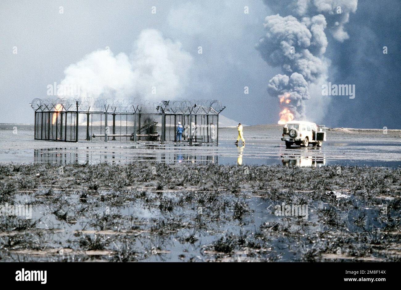 Un fuoco di petrolio brucia sullo sfondo, mentre i vigili del fuoco ispezionano un altro pozzo danneggiato ritirando le forze irachene durante l'operazione Desert Storm. Subject Operation/Series: DESERTO TEMPESTA Nazione: Kuwait(KWT) Foto Stock