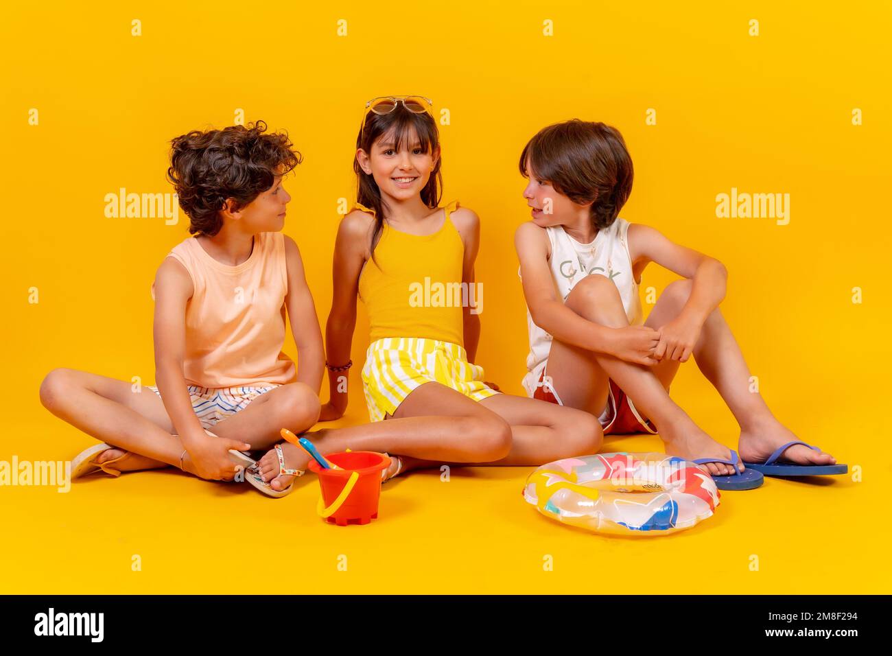 Bambini seduti sul pavimento godendo le vacanze con giocattoli, sfondo giallo Foto Stock