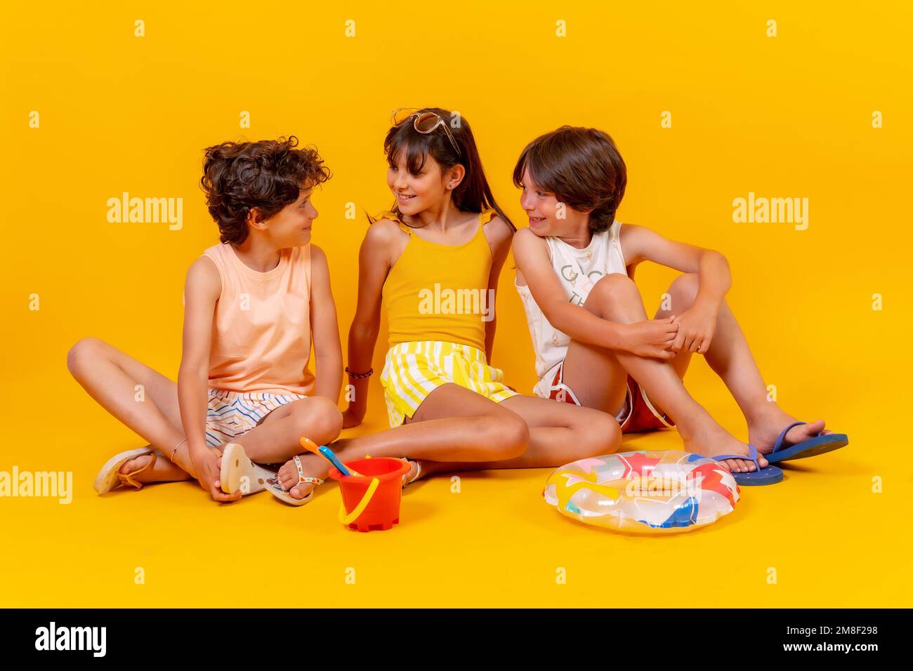 Ritratti di bambini seduti sul pavimento godendo di vacanze con giocattoli, sfondo giallo Foto Stock