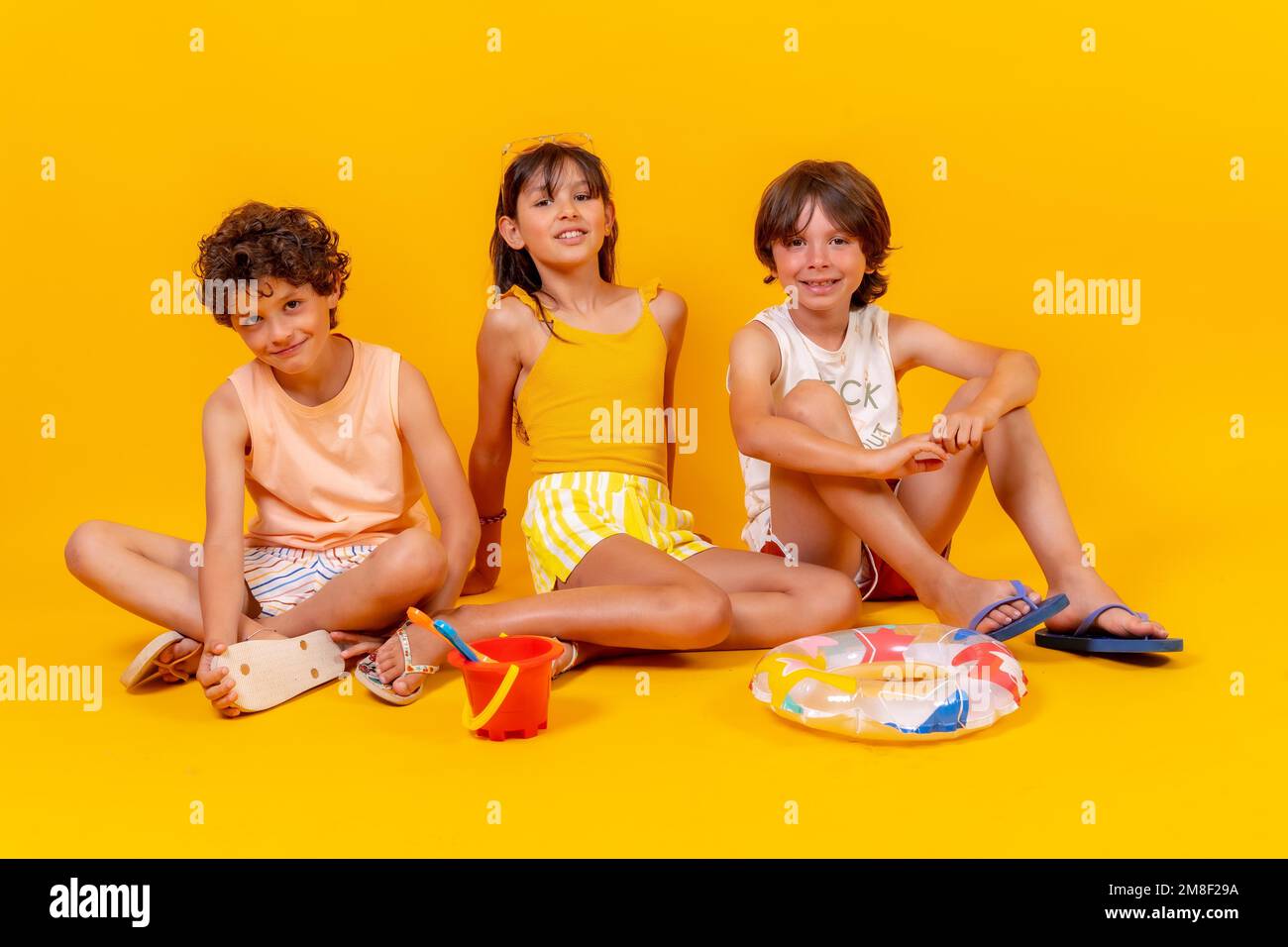 Ritratti di fratelli seduti sul pavimento godendo le vacanze con giocattoli, sfondo giallo Foto Stock