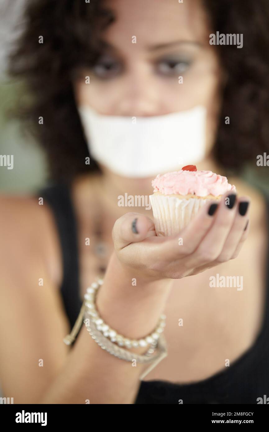 Dire no allo zucchero. Una giovane donna che tiene prodotti da forno con la bocca coperta. Foto Stock