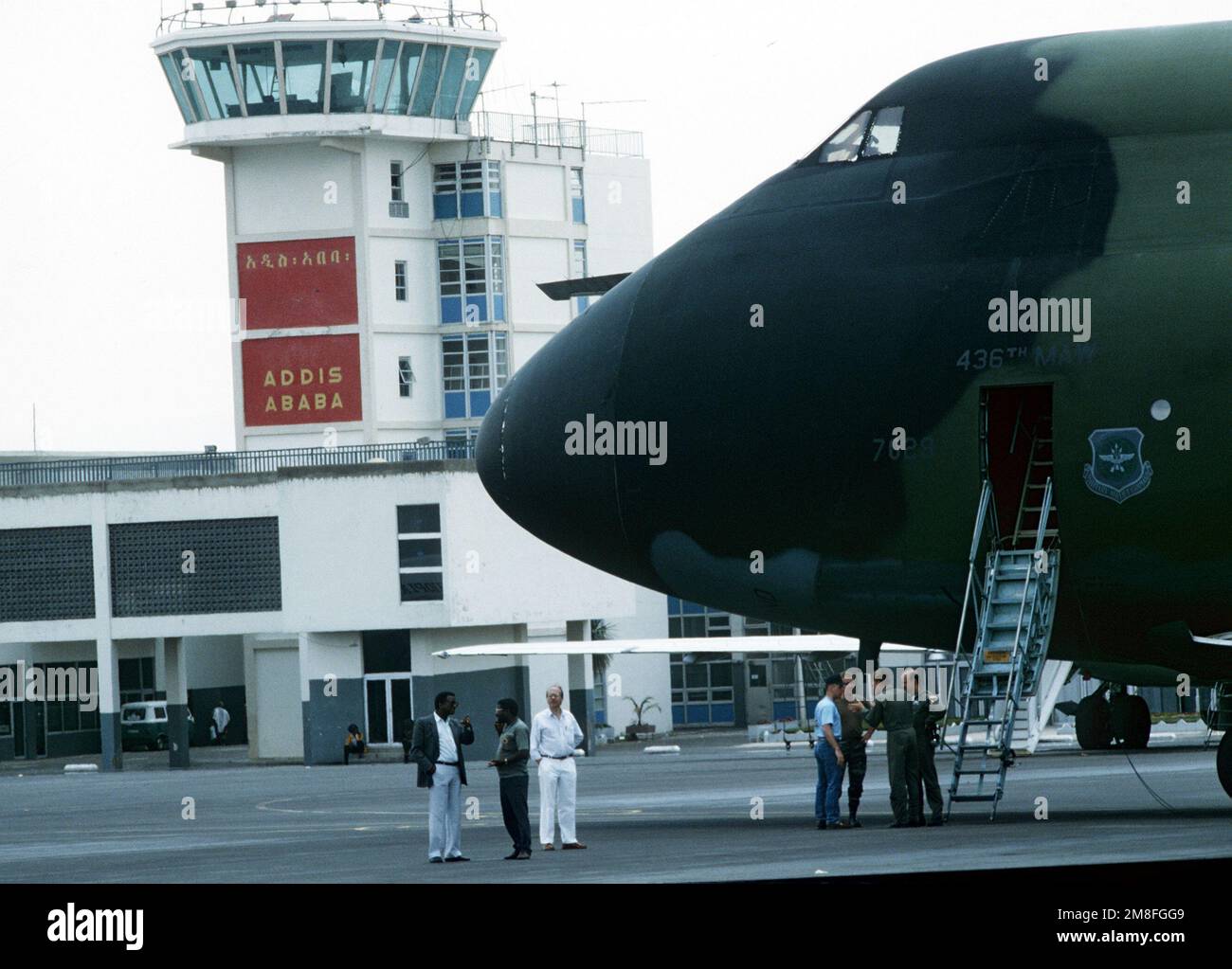 I membri dell'equipaggio e i rappresentanti della Croce Rossa conversano vicino al naso di un aereo militare del comando Airlift C-5A Galaxy dopo il suo arrivo con una spedizione di pasti pronti per mangiare (MREs). Le forniture vengono consegnate alla Croce Rossa che, a sua volta, le distribuirà ai rifugiati che soffrono a causa dei disordini civili dell'Etiopia. Gli MREs sono forniture militari in eccesso e sono messi a disposizione dall'autorità del programma McCallum e del programma DOD Excess Property. Base: Addis Ababa Paese: Etiopia(ETH) Foto Stock