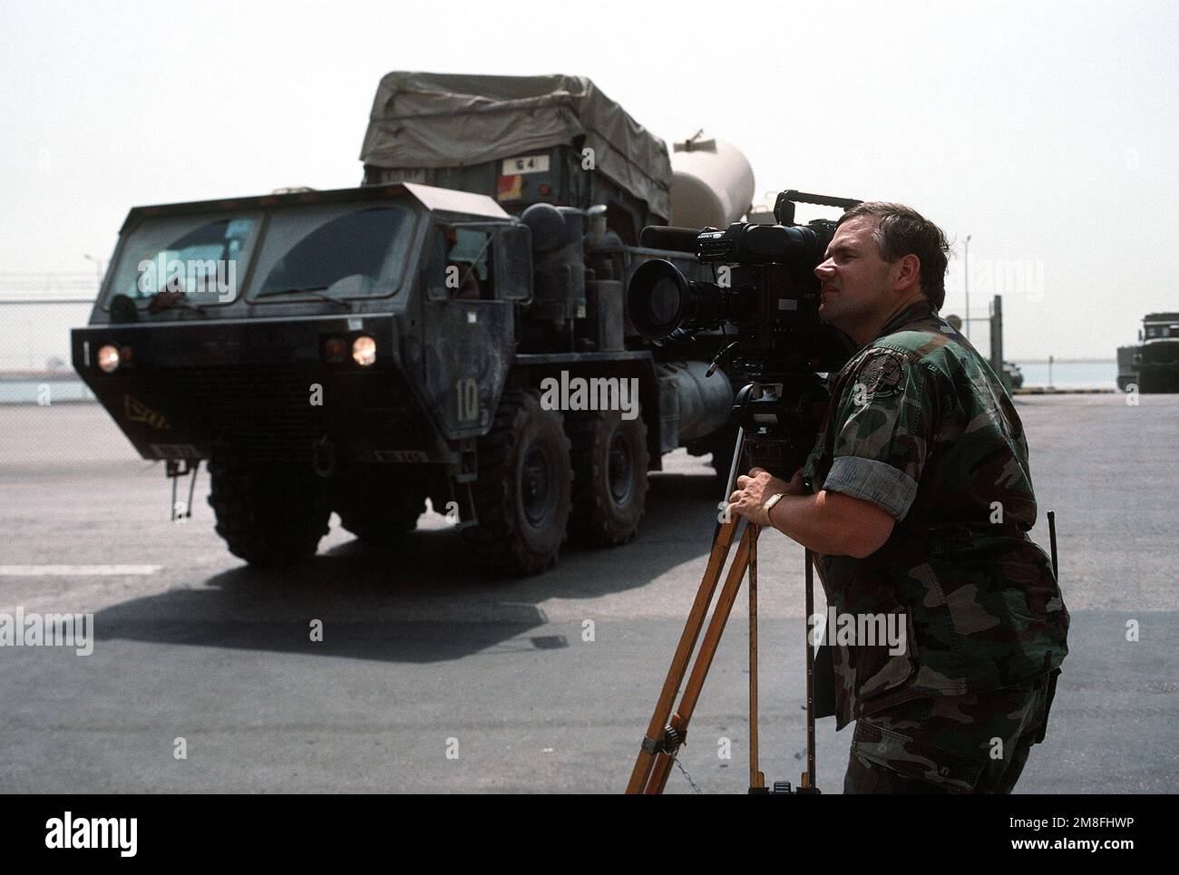 Un video cameraman filma accanto a un camion tattico di mobilità estesa pesante di Oshkosh M-977 mentre l'attrezzatura viene caricata a bordo di navi da carico militari Sealift Command. Attrezzature e ordigni vengono ridistribuiti negli Stati Uniti dopo l'operazione Desert Storm. Soggetto operativo/Serie: TEMPESTA DEL DESERTO Paese: Arabia Saudita (SAU) Foto Stock Un video cameraman filma accanto a un camion tattico di mobilità estesa pesante di Oshkosh M-977 mentre l'attrezzatura viene caricata a bordo di navi da carico militari Sealift Command. Attrezzature e ordigni vengono ridistribuiti negli Stati Uniti dopo l'operazione Desert Storm. Soggetto operativo/Serie: TEMPESTA DEL DESERTO Paese: Arabia Saudita (SAU) Foto Stock