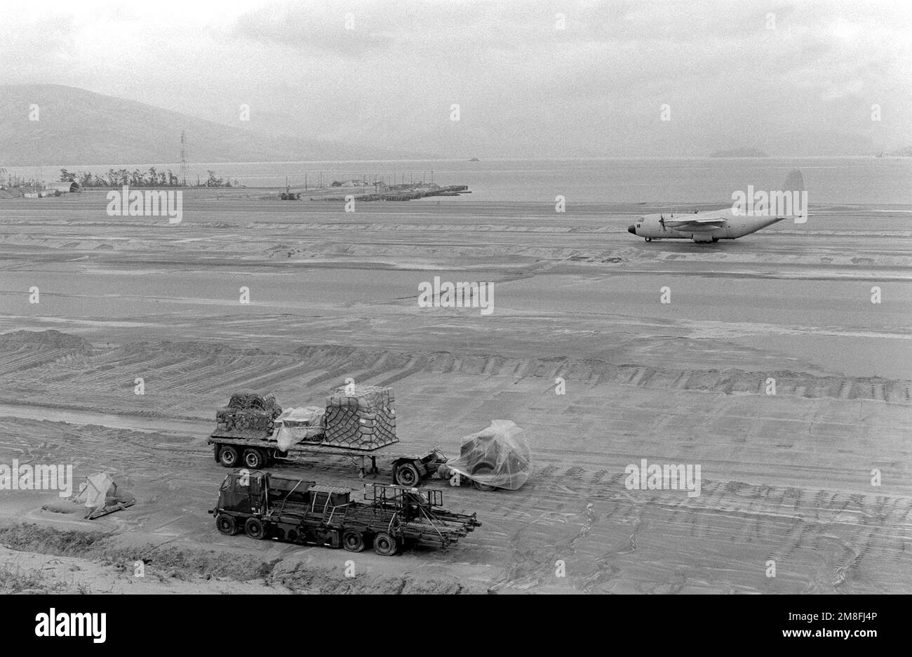 Rimorchi con materiale da costruzione, primo piano, e un aereo C-130 Hercules, sfondo, si trovano su un campo d'aviazione dopo che gli automobilisti hanno parzialmente pulito l'area delle ceneri dopo l'eruzione del Monte Pinatubo, un vulcano che è venuto in vita il 10th giugno per la prima volta in oltre 600 anni. Base: Naval Air Station, Cubi Point Paese: Filippine Foto Stock