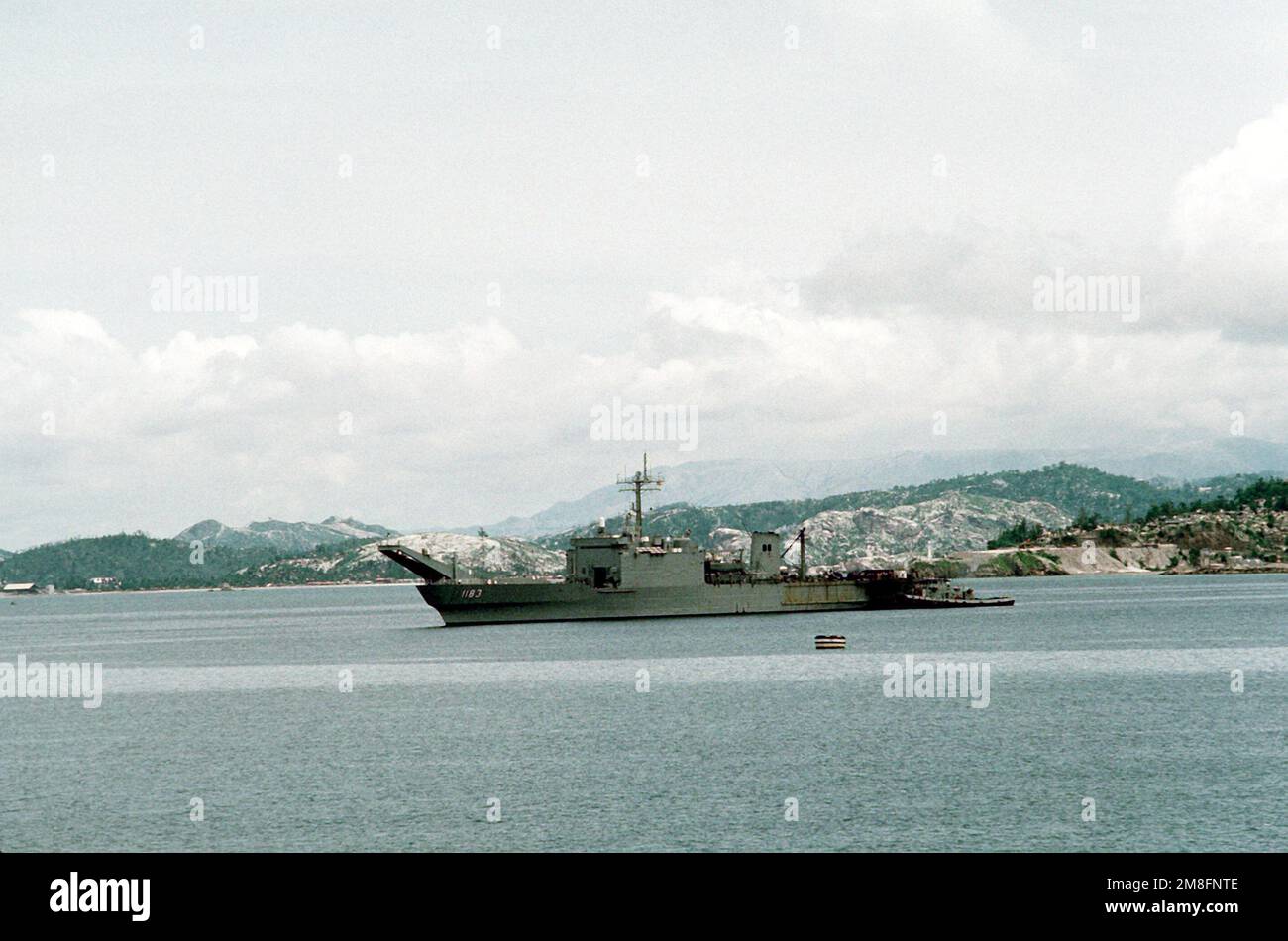 Un grande rimorchiatore del porto si trova accanto alla nave cisterna USS PEORIA (LST-1183) quando la nave arriva alla stazione navale. Le ceneri vulcaniche della recente eruzione del Monte Pinatubo coprono gran parte del paesaggio sullo sfondo. Base: Naval Station, Subic Bay Stato: Luzon Paese: Philippines(PHL) Foto Stock