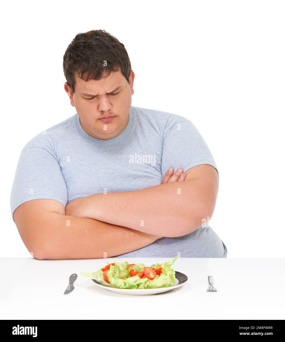 Non c'è stato tempo per l'insalata. Un giovane obese seduto con le braccia ripiegato su un tavolo con un piatto di insalata davanti a lui. Foto Stock