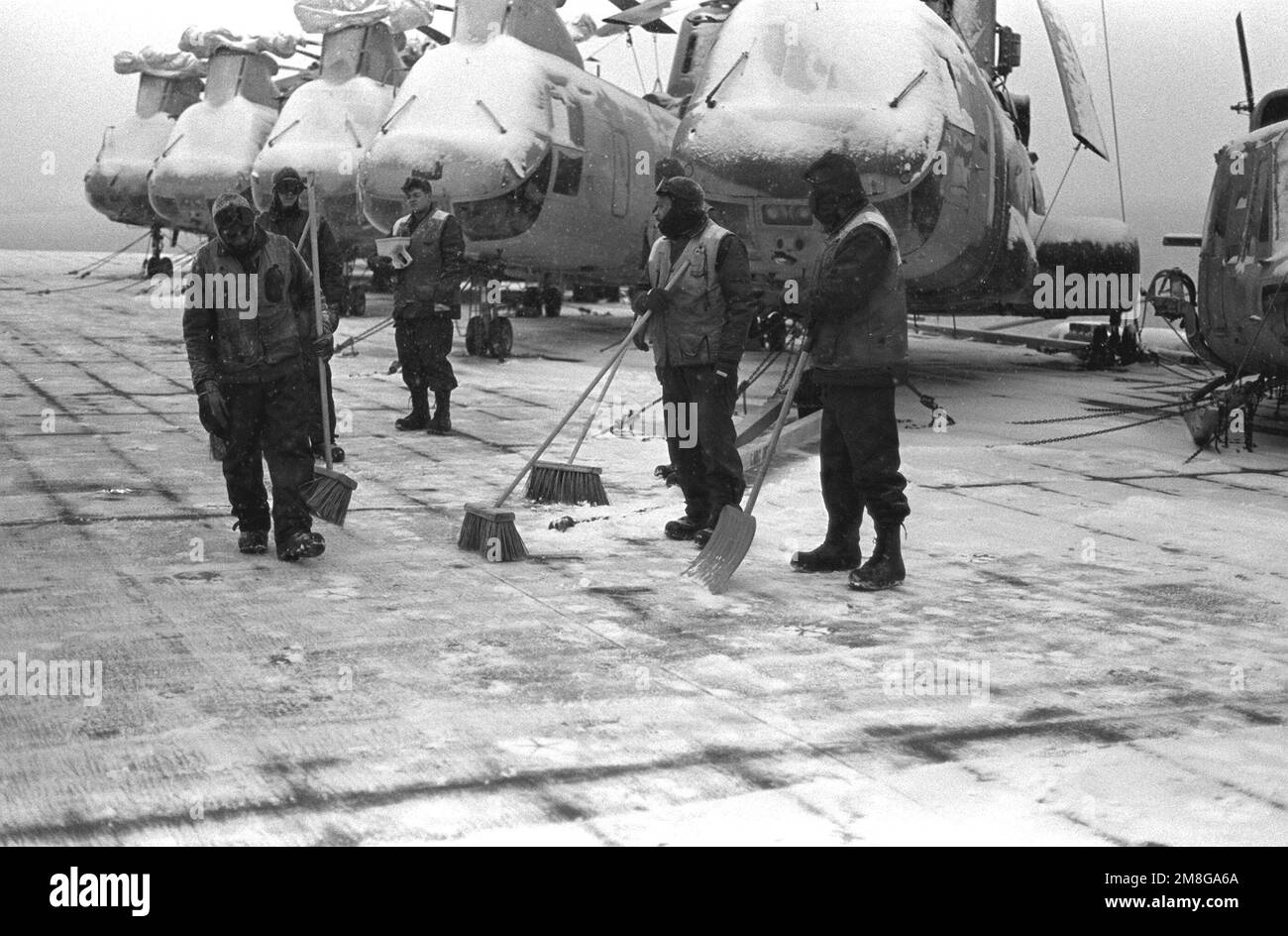 Diversi crewmen prendono una pausa dall'utilizzo di scope e pale a spinta per sgombrare la neve dal ponte di volo della nave d'assalto anfibio USS GUADALCANAL (LPH-7) mentre prendono parte alle operazioni invernali come parte dell'esercizio NATO Teamwork '92. Subject Operation/Series: LAVORO DI SQUADRA '92 base: Trondheim Fjord Paese: Norvegia (NOR) Foto Stock