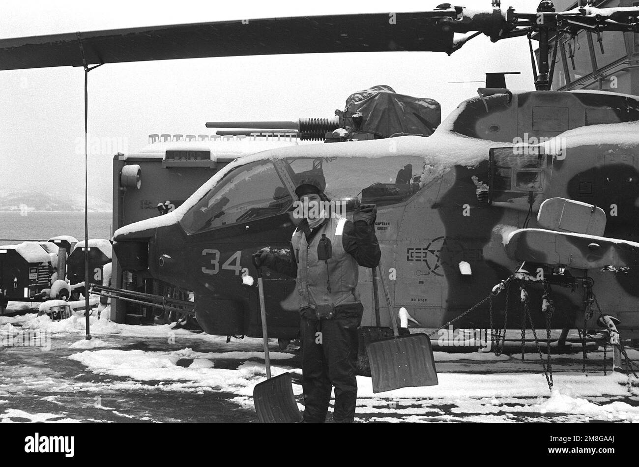 Un equipaggio di ponte di volo, con due pale da neve, posa per una fotografia accanto ad un elicottero AH-1W Super Cobra sul ponte di volo dell'assalto anfibio USS GUADALCANAL (LPH-7). Il doppio cilindro 3 pollici / 70 calibro di montaggio pistola in cima alla helo è effettivamente di fronte al ponte della nave. Il GUADALCANAL sta partecipando alla fase di chiusura dell'esercizio NATO Teamwork '92. Soggetto operativo/Serie: LAVORO DI SQUADRA '92 Paese: Norwegian Coast Foto Stock