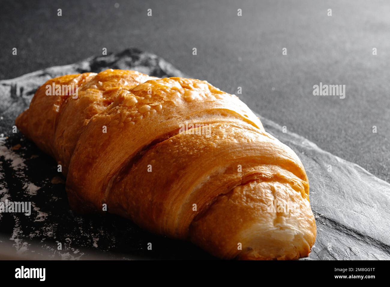 Grande croissant su sfondo nero. Pasticceria francese fresca e deliziosa, concetto di panetteria, immagine ravvicinata Foto Stock