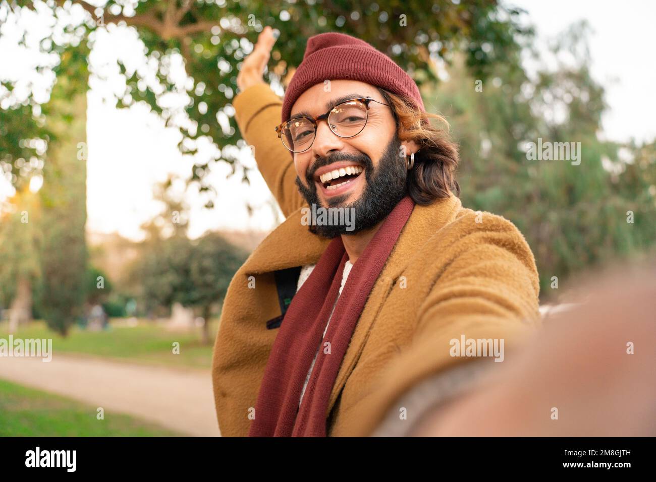 Felice giovane uomo caucasico con bicchieri e barba prendendo un selfie all'aperto nel parco in inverno. Foto Stock