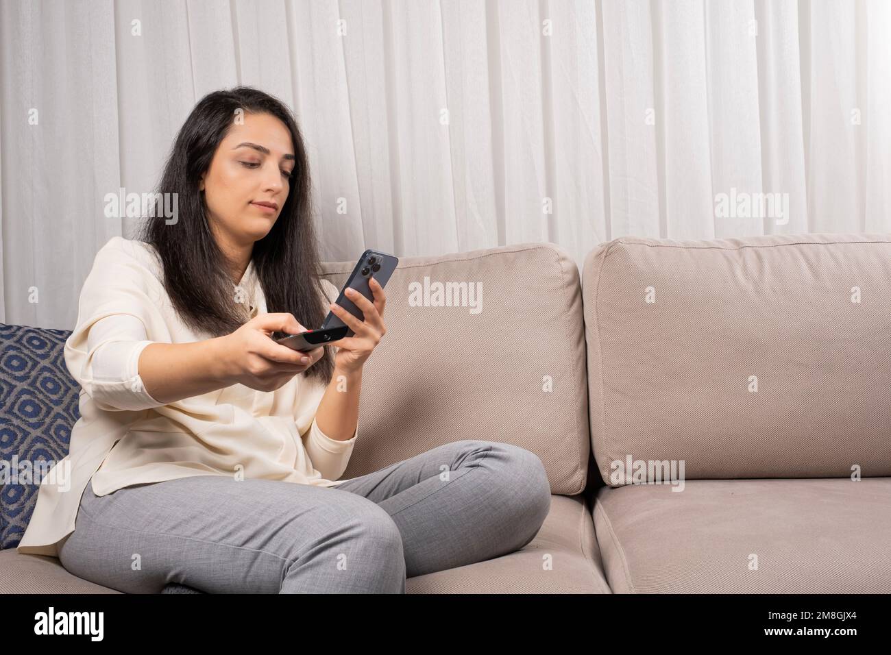 Donna con telecomando tv, guarda smartphone hanno dipendenza dai social media. Il divano di casa vuole guardare la televisione. Idea di concetto di zapping. Foto Stock