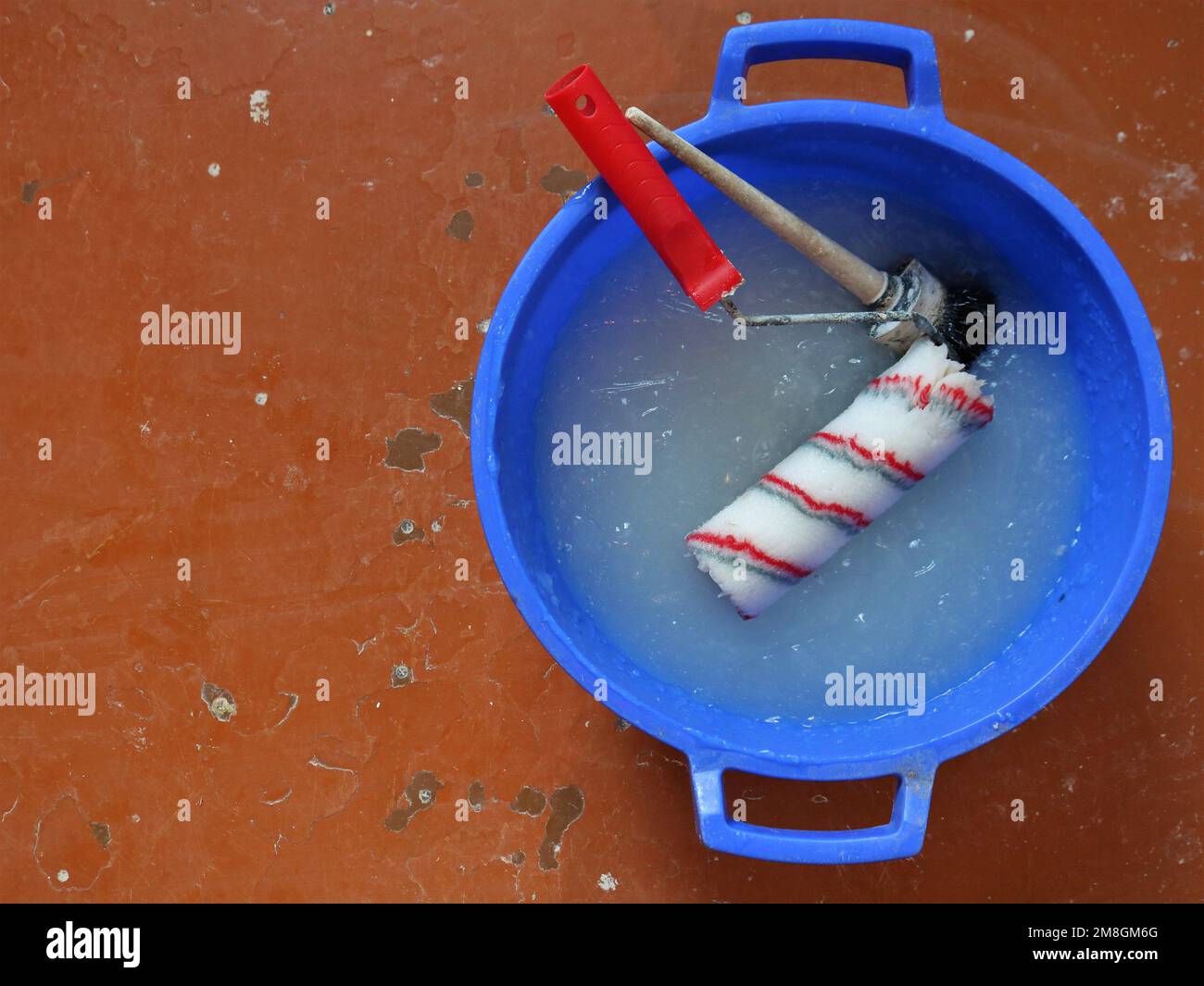 riparare lo sfondo del lavoro con una vasca di plastica blu riempita con colla spessa per tappezzeria e una spazzola rotonda nera e un rullo rosso e bianco Foto Stock