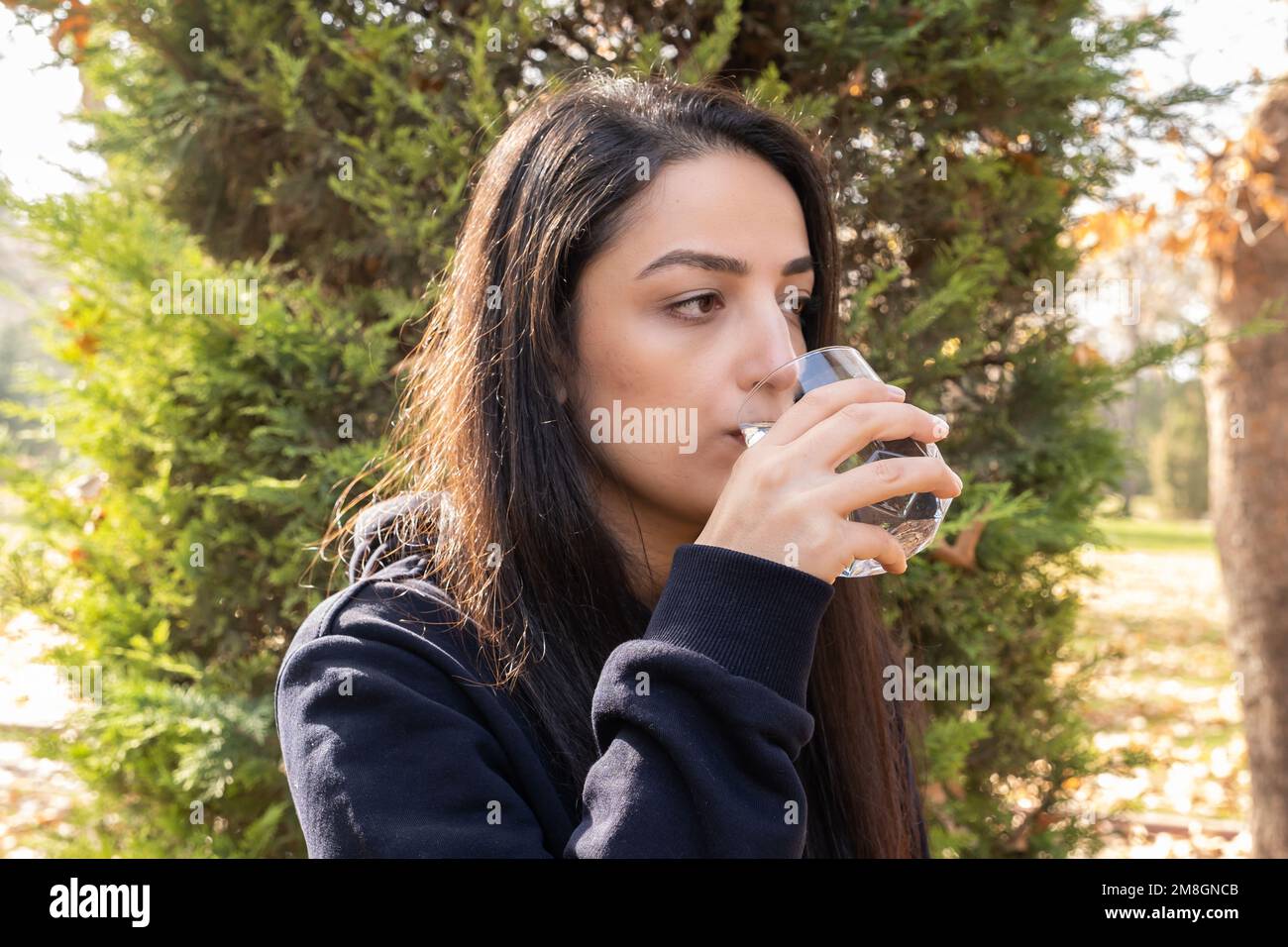 Sete disidratata donna bevendo bicchiere d'acqua. All'aperto, giorno d'autunno. Sfondo verde della struttura, spazio di copia. Sana abitudine, concetto di stile di vita idea. Foto Stock