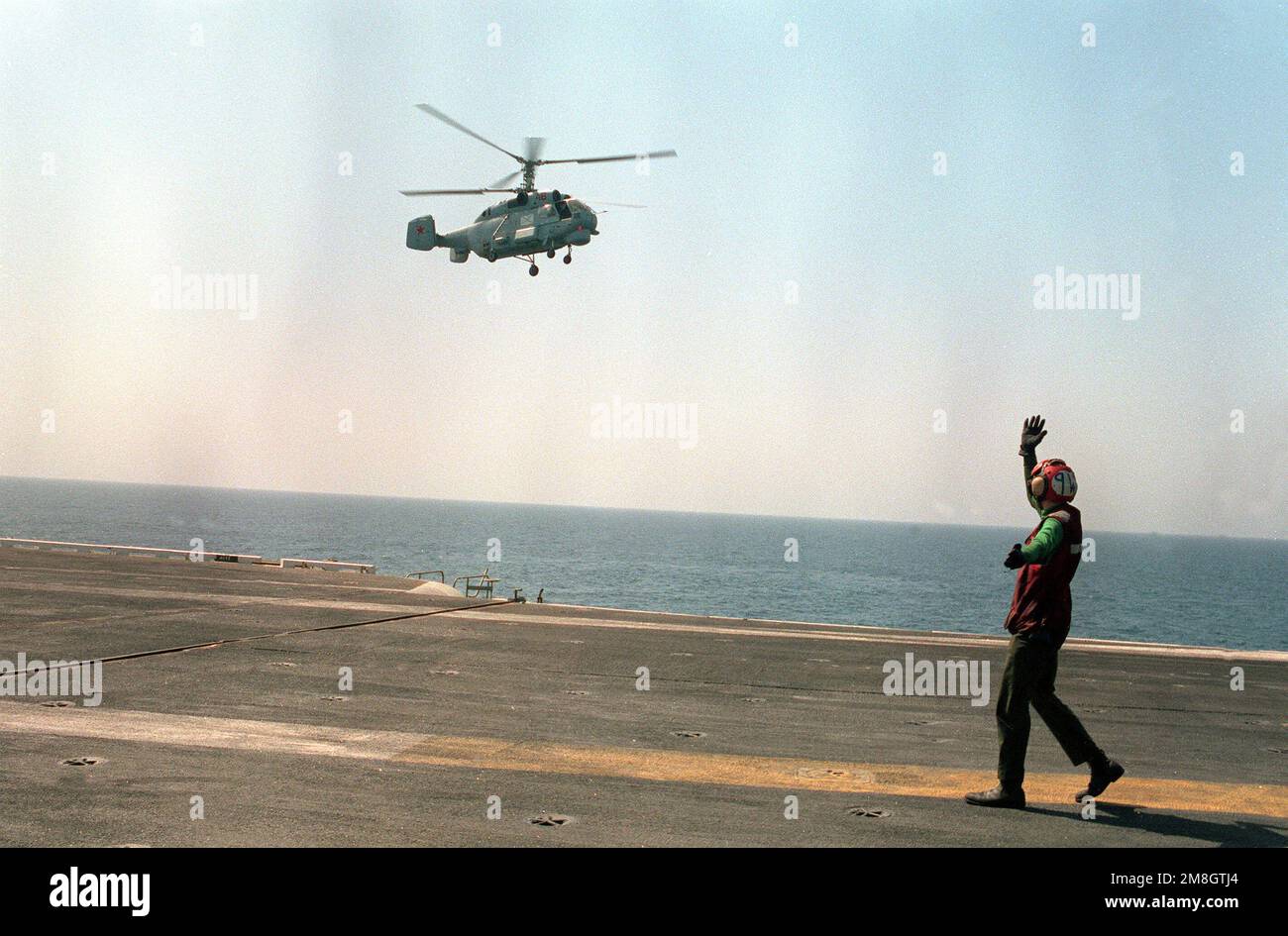 Un membro dell'equipaggio del ponte di volo segnala al pilota di un elicottero Ka-27 Helix quando si avvicina alla portaerei USS RANGER (CV-61) in preparazione dell'atterraggio a bordo della nave. L'Helix proviene dal cacciatorpediniere missilistico guidato Ammiraglio Vinogradov (BPD-554) che, insieme al RANGER, fa parte di una forza navale multinazionale che partecipa alle esercitazioni nella regione. Nazione: Mar Arabico Settentrionale Foto Stock