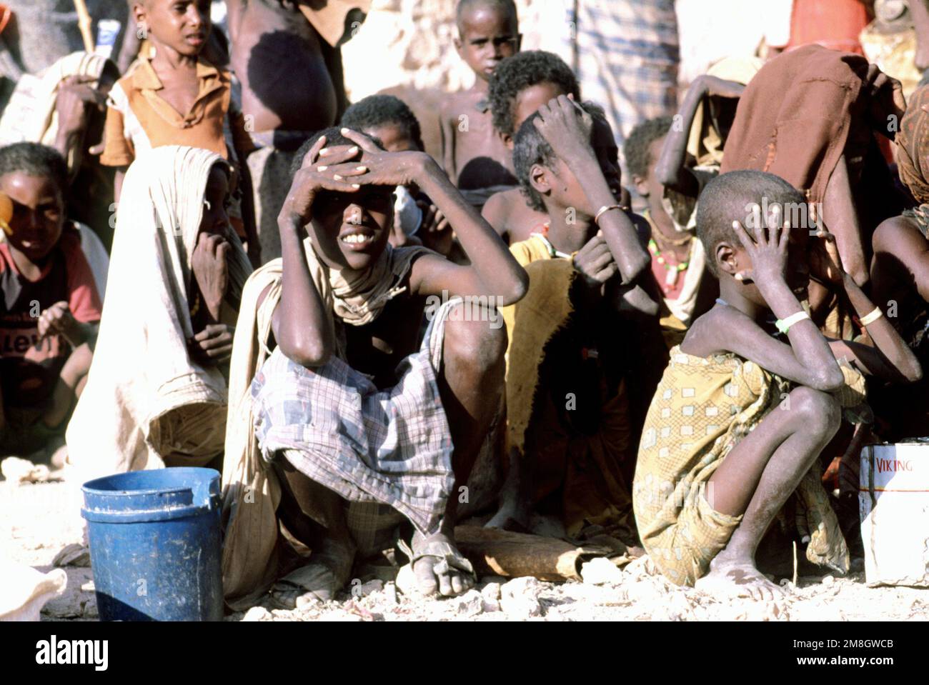 I somaliani si siedono al sole mentre attendono il cibo fornito durante l'operazione fornire soccorso, Somalia. Questo segnale è stato uno dei tanti punti di vista presi in considerazione da una delegazione del Congresso. I delegati, diretti dal Rep. John Lewis (D-GA) e dal Rep. Bill Emerson (D-MO), hanno visitato diversi siti di soccorso umanitario per determinare l'impatto degli aiuti statunitensi nel paese assediato. Oggetto operazione/Serie: FORNIRE SOCCORSO Paese: Somalia (SOM) Foto Stock